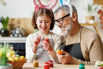 Happy little girl dyeing Easter eggs with Grandpa